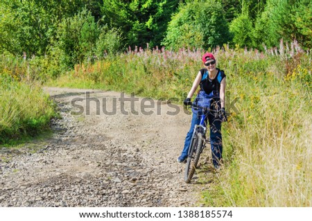 Beautiful,  joyful young woman stands with a Bicycle on a forest mountain road on a summer Sunny day