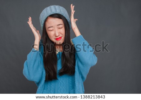A beautiful Korean girl in a blue sweater and blue hat is wriggling in front of the camera. studio photo shoot, girl posing.