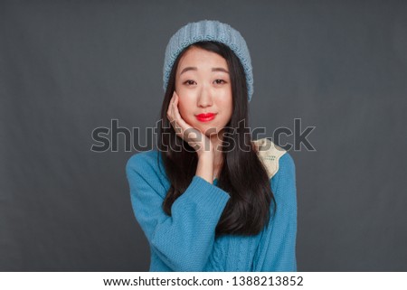 A beautiful Korean girl in a blue sweater and blue hat is wriggling in front of the camera. studio photo shoot, girl posing.