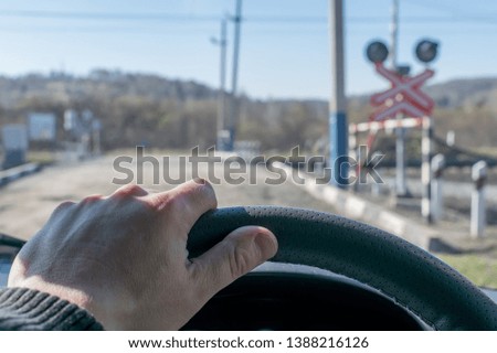 View of the driver's hand on the steering wheel of the car, which stopped before the railway crossing and indicator road signs