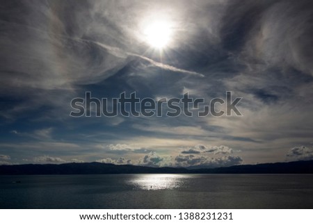 Landscape of a mystically cloudy sky with reflected sun in the silver waters of Ohrid Lake. Northern Macedonia.