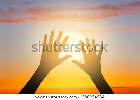 Two woman's silhouette hands on the beautiful sunset sky above the sea. The image pictures the concept of hope, faith, religion, life, relationship, love, friendship and care.