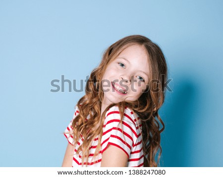 pretty girl with curly hair and red white striped shirt is posing in front of blue background