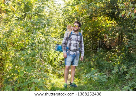 Hike, tourism and nature concept - Young traveler with backpack and with his cat standing over forest background