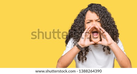Young beautiful woman with curly hair wearing white t-shirt Shouting angry out loud with hands over mouth