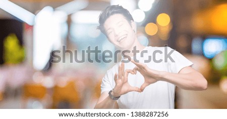 Young handsome man wearing casual white t-shirt over isolated background smiling in love showing heart symbol and shape with hands. Romantic concept.