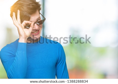 Young man wearing funny thug life glasses over isolated background doing ok gesture with hand smiling, eye looking through fingers with happy face.