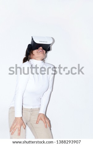 In glasses-mask with virtual effects, the girl in funny pose Immersed  three-dimensional space with the effect of personal presence, she laughs in admiration, stands on a white background 