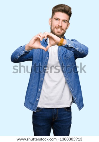 Young handsome blond man wearing casual denim jacket smiling in love showing heart symbol and shape with hands. Romantic concept.