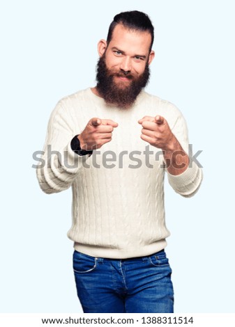 Young hipster man wearing winter sweater pointing fingers to camera with happy and funny face. Good energy and vibes.