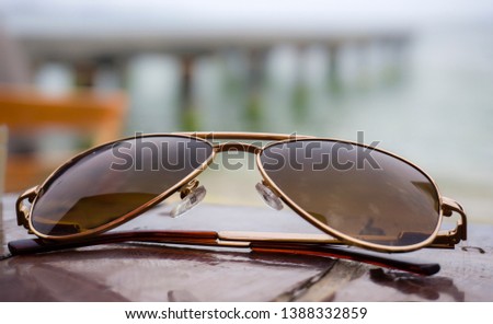 Sunglasses closeup on the table on beach towards sea and coast pier. Holiday, vacation and relaxation conceptual photography. Close up / Low view of a retro or modern sunglasses at seaside or shore.