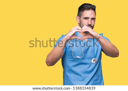 Handsome young doctor surgeon man over isolated background smiling in love showing heart symbol and shape with hands. Romantic concept.