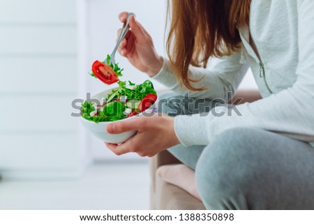Healthy woman in sportswear holding a bowl of fresh vegetable salad at home. Balanced organic diet and clean fitness eating.  Royalty-Free Stock Photo #1388350898