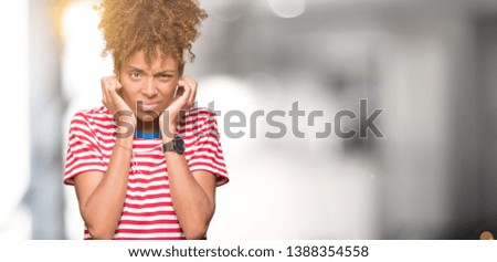 Beautiful young african american woman over isolated background covering ears with fingers with annoyed expression for the noise of loud music. Deaf concept.