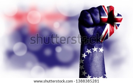 Flag of Cook Islands painted on male fist, strength,power,concept of conflict. On a blurred background with a good place for your text.