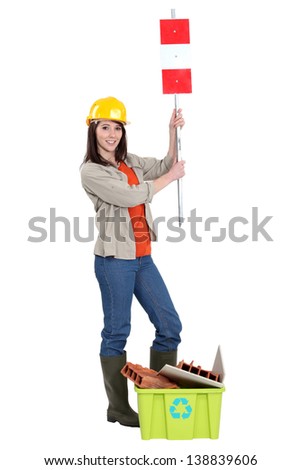 Tradeswoman holding up a traffic sign behind a recycling bin