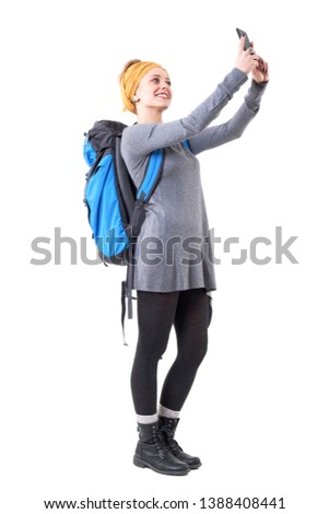 Relaxed happy traveling young woman with rucksack taking selfie with smartphone. Full body isolated on white background. 