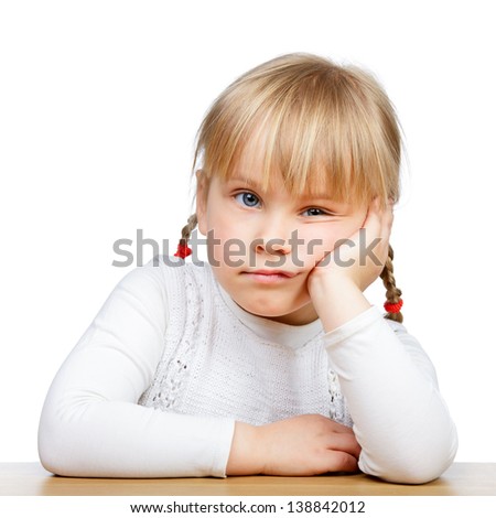 Portrait of unhappy little girl sitting at desk with hand on chin