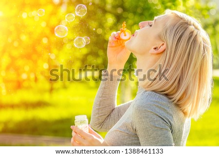 attractive blonde girl blowing soap bubbles in the park on a background of green grass . bubble and holiday atmosphere