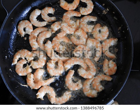 Closeup top view of cooking shrimp/prawns on a round iron cast frying pan with butter and garlic