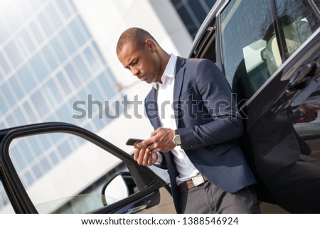 Young african american man standing leaning on car browsing smartphone working online concentrated