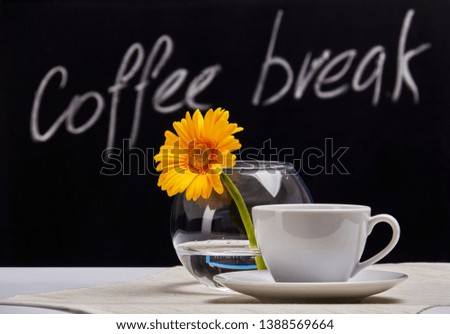 Cup of coffee and bowl of gerberas on a background of graphite Board with the inscription "Coffee break".