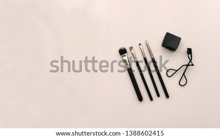 A basic set of make up brushes, eye lash curler and sharpener placed on a light beige peachy background. A ideal commercial photo for promoting a make up school with a lot of space for copy or design.