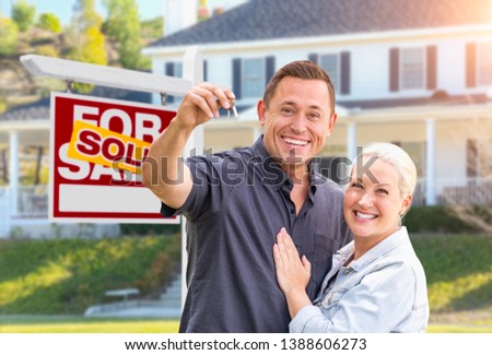 Happy Couple With New House Keys In Front of Sold Real Estate Sign and Beautiful House.