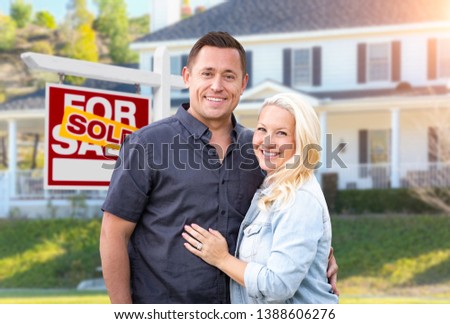 Happy Couple In Front of Sold Real Estate Sign and Beautiful House.