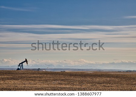 A lone oil pumping jack on a field of farm land with the Rockies at the background.