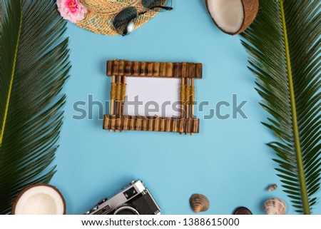 Stylish summer composition with photo frame, green leaves, hat and sunglasses on a blue pastel background. Artwork mockup with copy space