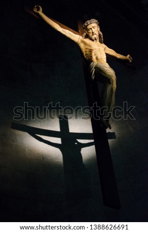 Antique wooden crucifix illuminated inside a historic Italian church with shadow cast on the wall