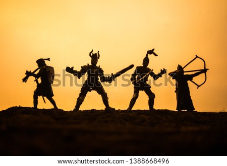 Medieval battle scene with cavalry and infantry. Silhouettes of figures as separate objects, fight between warriors on sunset foggy background. Selective focus