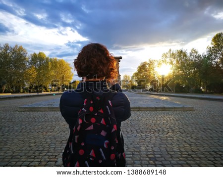 Woman taking a photograph of the temple of Debod in Madrid, Spain. Sunset as background. Cloudy sky. 