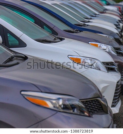 A colorful row of new cars sits awaiting buyers in an auto dealer parking lot, some out of focus