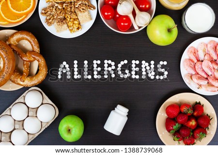Food allergens as milk, oranges, tomatoes, garlic, shrimp, peanuts, eggs, apples, bread, strawberries on wooden table. Royalty-Free Stock Photo #1388739068