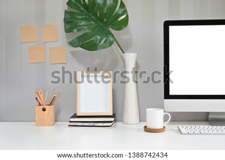 Workspace with computer, coffee mug, pencil and photo frame with sticky note on the wall.