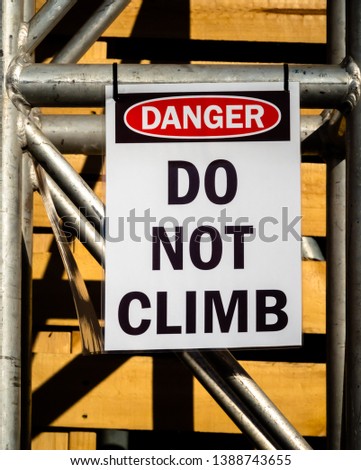 Laminated paper sign with the words DANGER DO NOT CLIMB hanging from temporary metal scaffolding in front of wood crates
