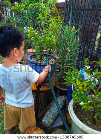 asian kid helping parents watering plant. using pipe hose to feed the flower pot. stock photo -image