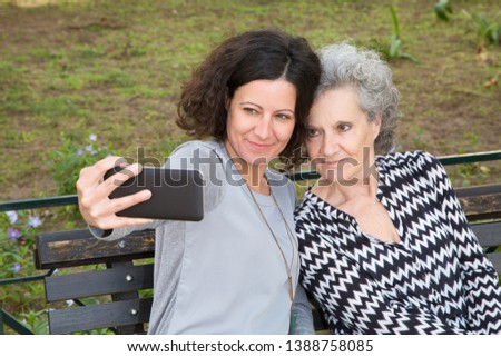 Positive relaxed young and elder woman posing for selfie outdoors. Mother and daughter picturing on smartphone in city park. Leisure or weekend outdoors concept