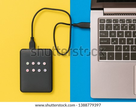 External hard drive connected to laptop on blue and yellow background. Flat lay. The concept of backup storage.