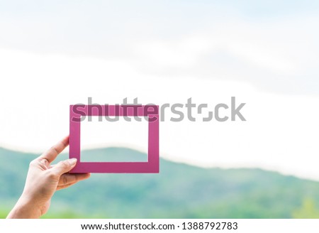 Hand  of  a  woman  holding  pink  wooden  picture  frame  with  nature  blurry  background