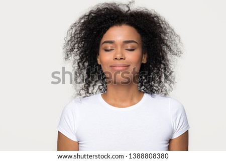 Head shot portrait mixed race attractive calm woman in white t-shirt isolated on grey background, closed eyes smile enjoy fresh air dreaming about future feels satisfied and tranquil conceptual image
