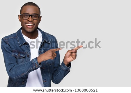 Cheerful african man wearing glasses jean jacket having white snow smile pointing fingers aside at copy space for your text advertisement, advertise teeth whitening or eyewear store good offer concept Royalty-Free Stock Photo #1388808521