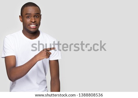 African man pointing finger aside at copy space look at camera showing something awkward and strange isolated on grey blank, concept of sneer shameful uncomfortable embarrassing Oops foolish situation Royalty-Free Stock Photo #1388808536