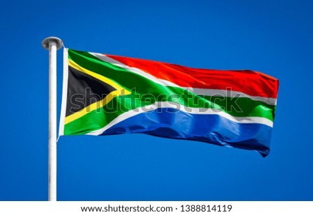 Flag of South Africa blowing in strong wing against pure blue sky. Symbol of national patriotism.
