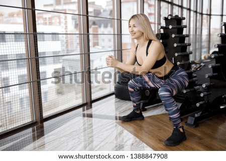 Beautiful young sportswoman standing and doing squats in gym. Active Lifestyle. Sports in the gym.
