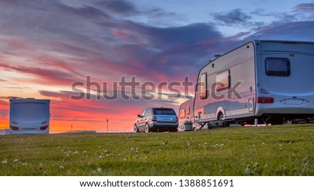 Camping caravans and cars parked on a grassy campground under beautiful sunset Royalty-Free Stock Photo #1388851691