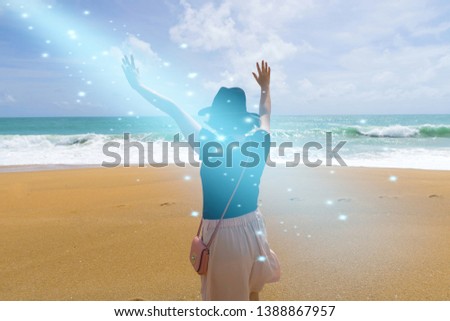 Surreal background with back side view of woman wore sun hat & lifted hands in magic sparkle light from sky at tropical summer ocean beach & waves, holiday vacation dream & freedom concept, copy space Royalty-Free Stock Photo #1388867957