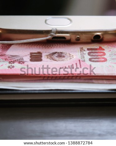 A smartphone on Thai baht banknote cash money , on wood background. Concept of online business/side income